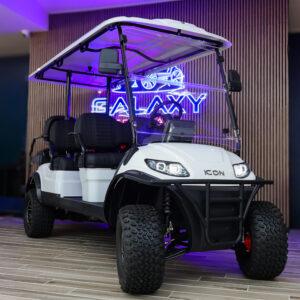 Front angle view of a white ICON 6-passenger lifted golf cart with off-road tires, clear windshield, and black seats at the Galaxy Golf Cars showroom