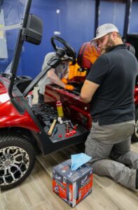 Galaxy Golf Cars technician performing electrical diagnostics and maintenance on a red electric golf cart in the service department