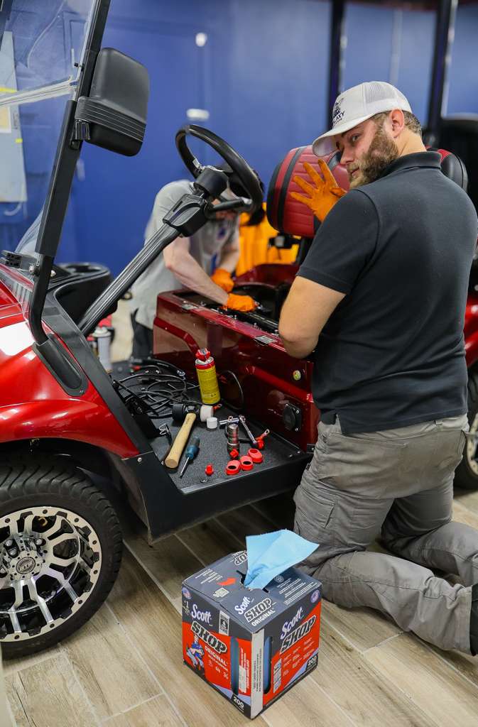 Galaxy Golf Cars technician performing electrical diagnostics and maintenance on a red electric golf cart in the service department