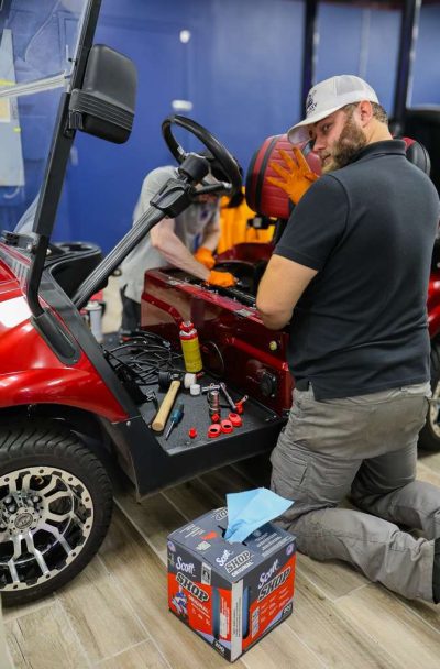 Galaxy Golf Cars technician performing electrical diagnostics and maintenance on a red electric golf cart in the service department
